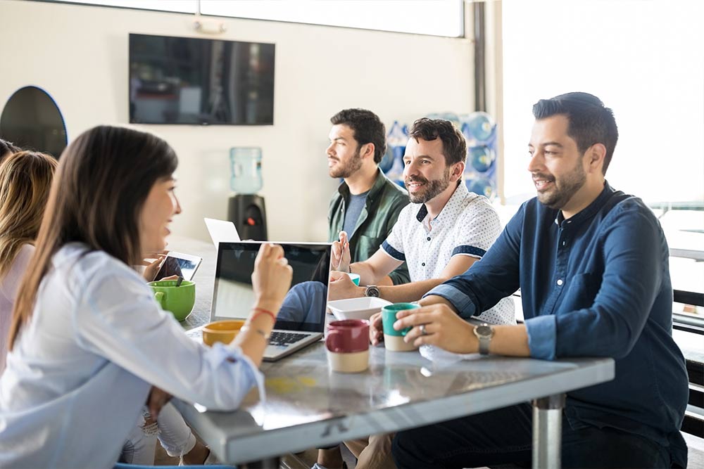 Empleados de una empresa sentados al rededor de una mesa conversando entre ellos